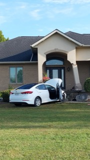 White sedan with damaged driver's side door, front lawn, two-story house