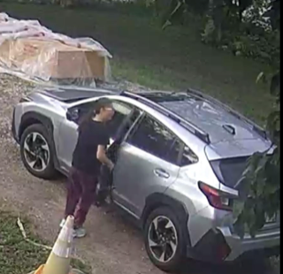 Silver SUV with damage to rear passenger side. Person in black shirt and dark pants standing near the vehicle.