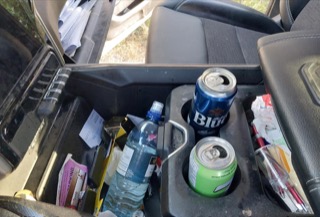Cluttered car console with a water bottle, beer cans, and a packet of cigarettes