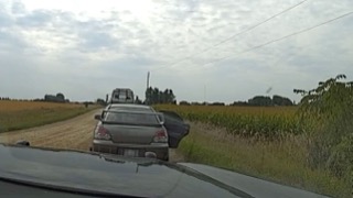 Two cars on a dirt road, cornfield in background