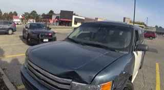 Damaged dark green SUV, police car visible in background