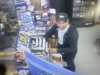 Man reaching for a bottle behind a display of drinks.
