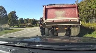 Red dump truck with a man standing on the rear.