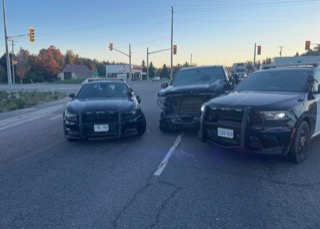 Two black police cars and a black sedan at a red light.