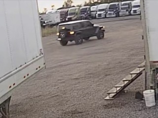 Black pickup truck driving on gravel lot, several white vans in background
