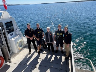 Four people in police uniforms and life vests stand on a boat deck.