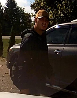 Person in a hoodie and baseball cap standing next to a dark SUV
