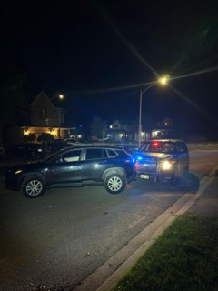 Two SUVs, one with flashing emergency lights, parked on a residential street at night.