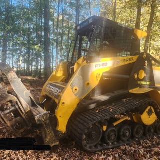 Yellow skid steer with black tracks, wooded background