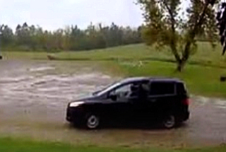 Black minivan driving through flooded field