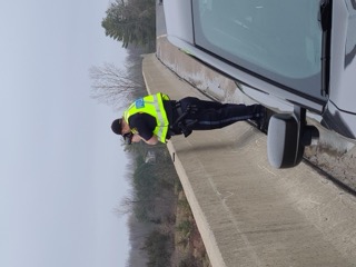 Police officer examining a vehicle on the side of a road.
