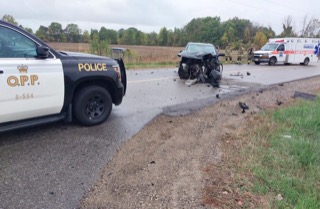 Two cars involved in a collision on a rural road. Police and ambulance are present. Debris scattered on the pavement.