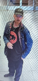 Man in a black t-shirt and jeans, wearing a dark green baseball cap and a blue denim jacket.