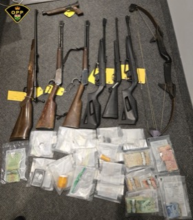 Several rifles and a bow and arrow, alongside packages of cash and a small amount of a leafy substance.