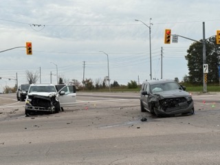 Two pickup trucks, damaged in a collision, block an intersection.
