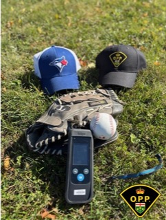 Blue baseball cap, black glove, baseball, and radar gun on grass