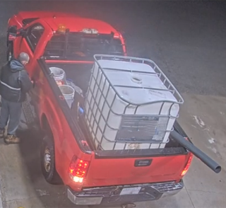 Red pickup truck with stacked plastic barrels in the bed.