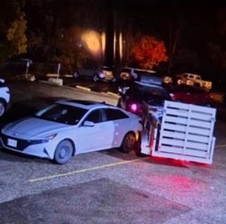 Damaged gray sedan with a white wooden pallet leaning against the driver's side.