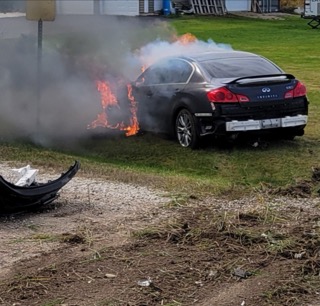 Black car engulfed in flames, smoke rising.