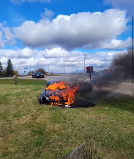Burning car on grass, black smoke rising