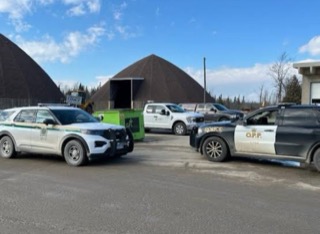 Two Quebec police vehicles parked in a lot, large piles of material in the background