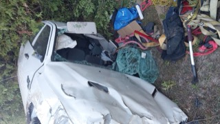 Damaged white car with shattered windshield and crushed hood.