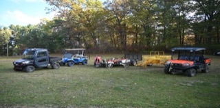 Two utility vehicles, a blue golf cart, a dirt bike, and a small trailer on grass.