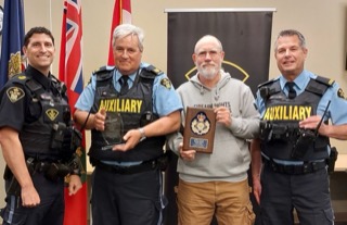 Four men in police uniforms and a gray hoodie holding a plaque.
