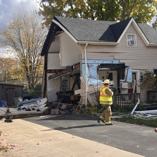 Damaged house with collapsed front porch, firefighter in yellow gear