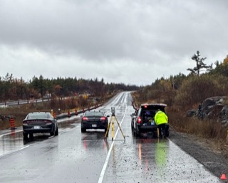 Wet highway with vehicles and a worker.