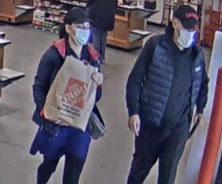 Two people wearing masks walk in a store, one carrying a Lowe's bag.