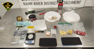 Scale with digital display, small glass jar, plastic baggies, knife, suspected drugs on a white surface