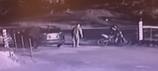 Man standing near a motorcycle, parked car visible in background.