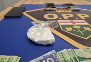 Pile of Canadian twenty-dollar bills and a bag of white powder. Ontario Provincial Police logo in background.