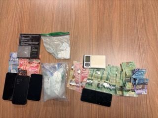 Two smartphones, a digital scale, clear plastic bags, and stacks of Canadian twenty-dollar bills on a wooden surface.