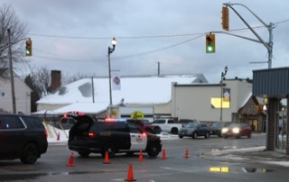 Police vehicles and traffic cones block a snowy street.