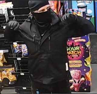 Person wearing a black hoodie and face mask stands in front of a candy display.