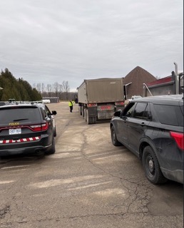 Police vehicle, dump truck, and SUV parked on a gravel lot