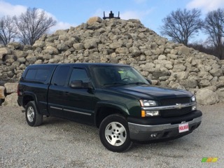 Dark green Chevrolet pickup truck with a camper shell, parked in front of a large pile of rocks