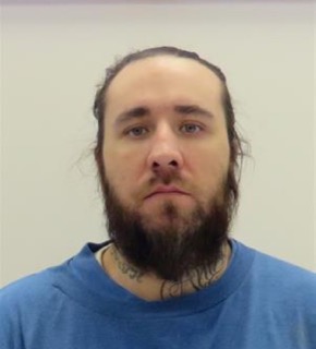 Man with a full beard and short hair, wearing a blue t-shirt, tattoos visible on neck