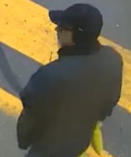 Person wearing a black baseball cap and dark clothing, standing on yellow and black striped pavement