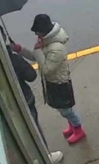 Person holding an umbrella, wearing a puffer jacket, dark skirt, jeans, and pink boots.