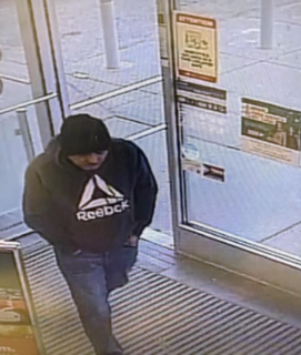 Person wearing a black Reebok hoodie and jeans walking toward a door.
