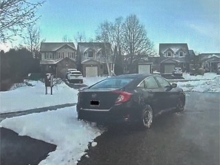 Black sedan in a snowy driveway, houses in background