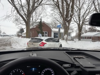 Car dashboard visible, snowy street ahead