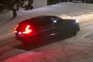 Car partially covered in snow, red brake lights illuminated