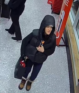 Person in a black puffer jacket and jeans, holding a small package.