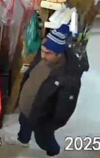 Man wearing a dark jacket, dark pants, and a blue and white striped hat.