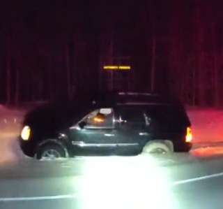 Black SUV driving on a snowy road, headlights illuminate the snow