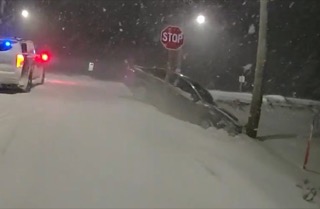 Car embedded in snowbank, stop sign visible, snow falling